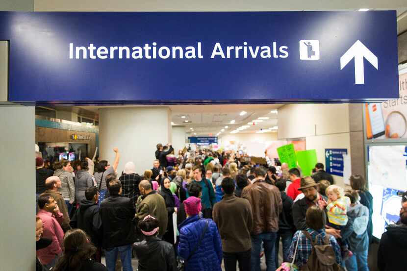 Protestors filled the international arrivals hall at DFW International Airport holds signs...