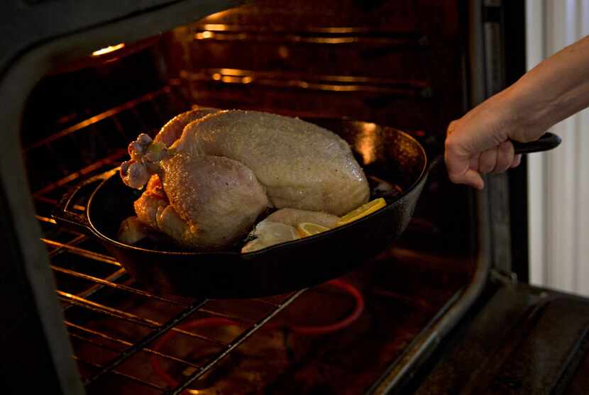 Rebecca White places a cast iron pan with a whole chicken in it into an oven Thursday, April...