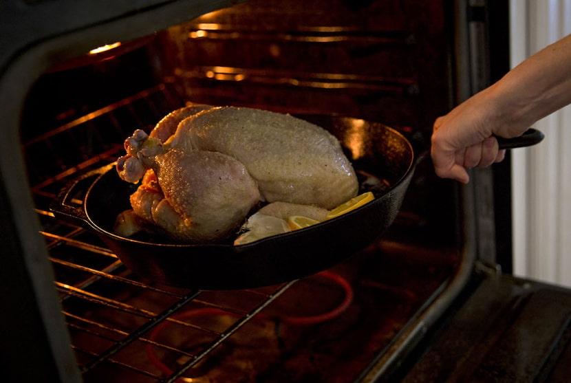 Rebecca White places a cast iron pan with a whole chicken in it into an oven Thursday, April...