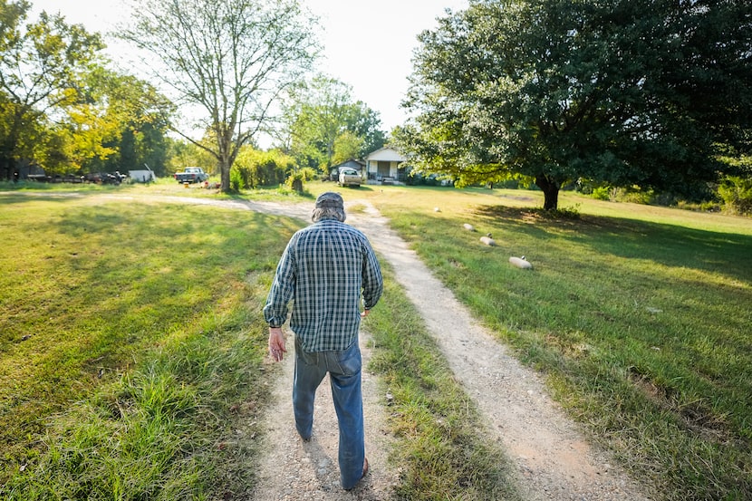 Dickie Dalby, 83, walks toward a small house that is built around a log cabin, which was...