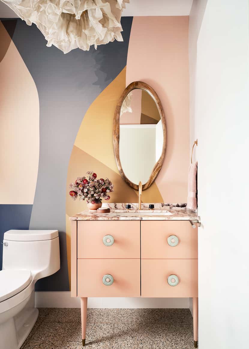 The powder room features a pink custom sink vanity, a wood mirror, and graphic wallpaper.