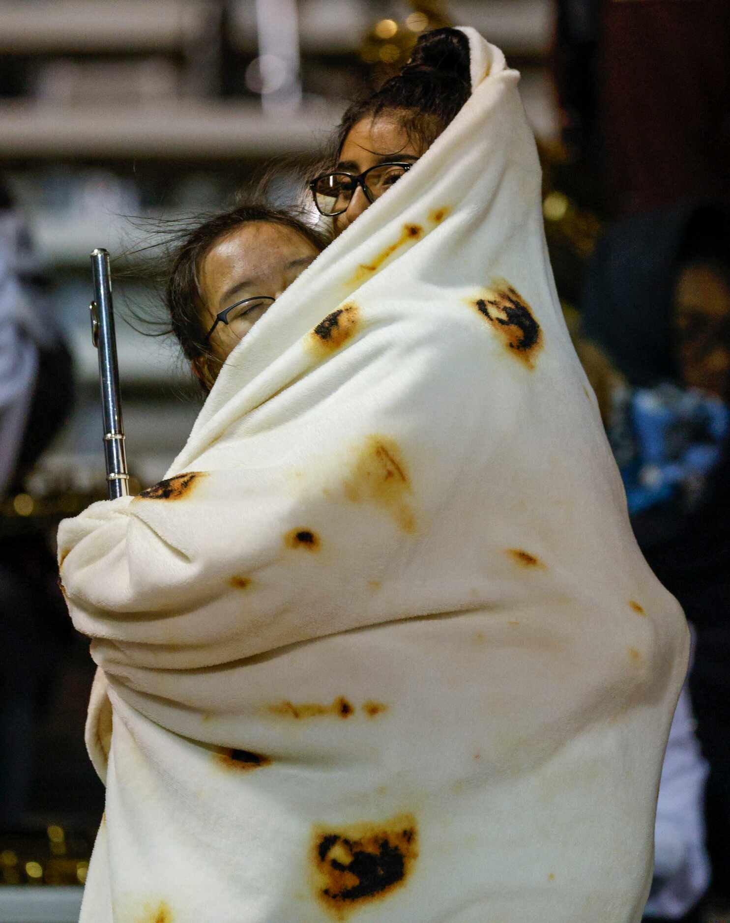 Members of the Lewisville marching band huddle together for warmth with a blanket during the...