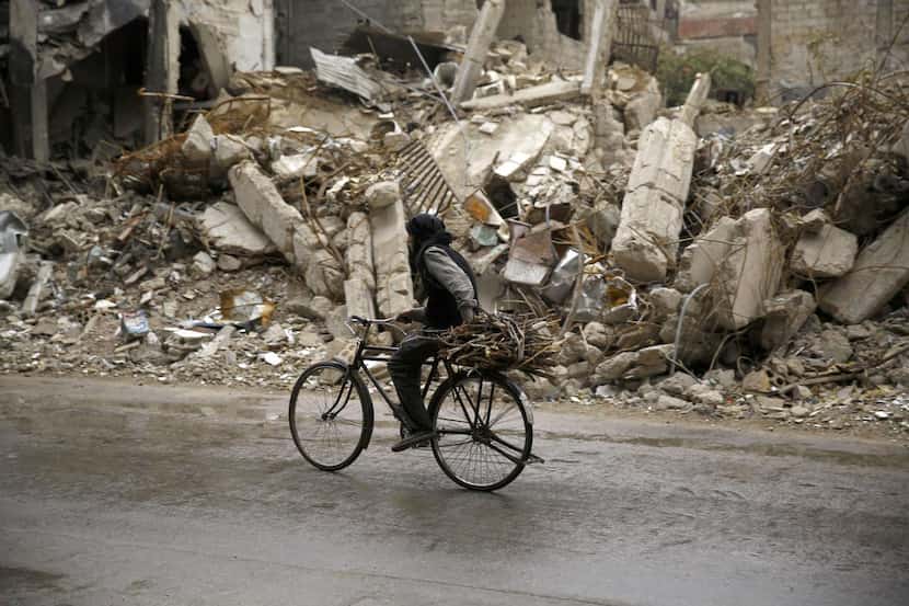 
A Syrian man rides a bike past damaged buildings in the rebel-held area of Douma, east of...