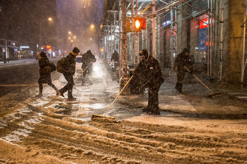 Workers sweep the streets as snow falls in the early morning hours in the East Village...