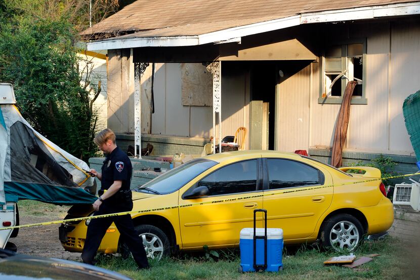 An Arlington police officer walks past a car and camper parked in front of a run-down house...