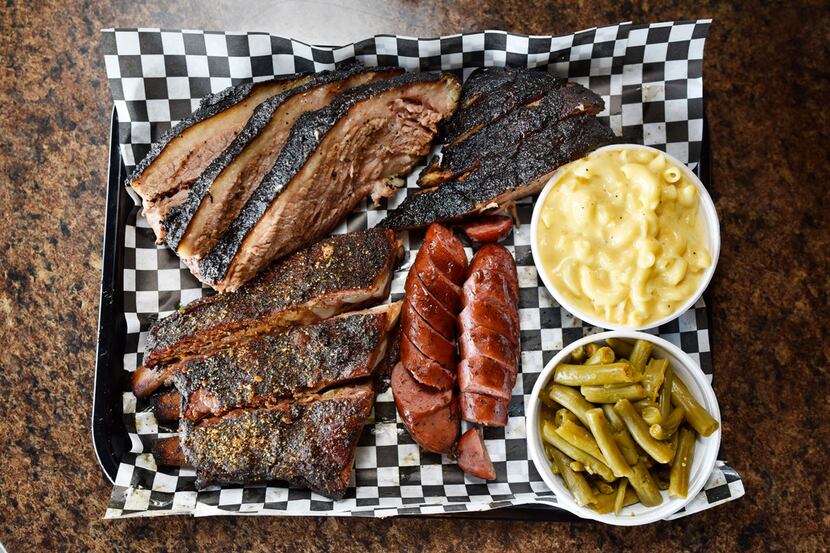 A platter of brisket, sausage, ribs, with sides of mac and cheese and green beans is...