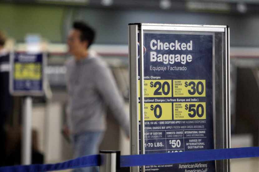  A traveler rolled luggageÂ past a sign displaying checked baggage fees on American Airlines...
