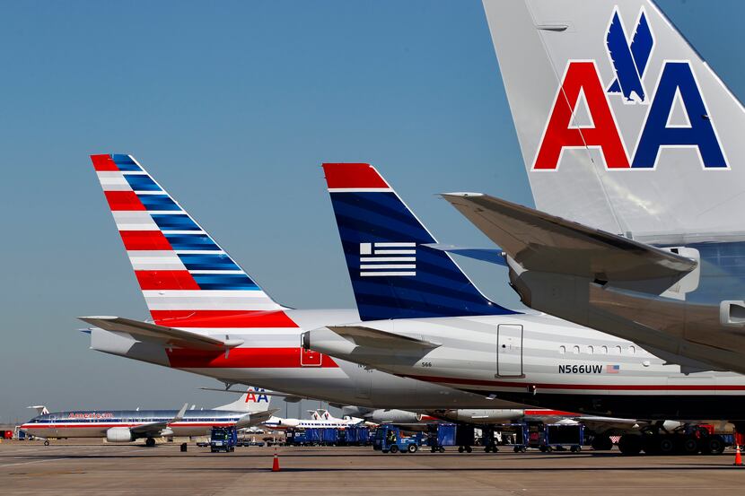 A US Airways plane is parked between two American Airlines planes, one bearing the new logo,...
