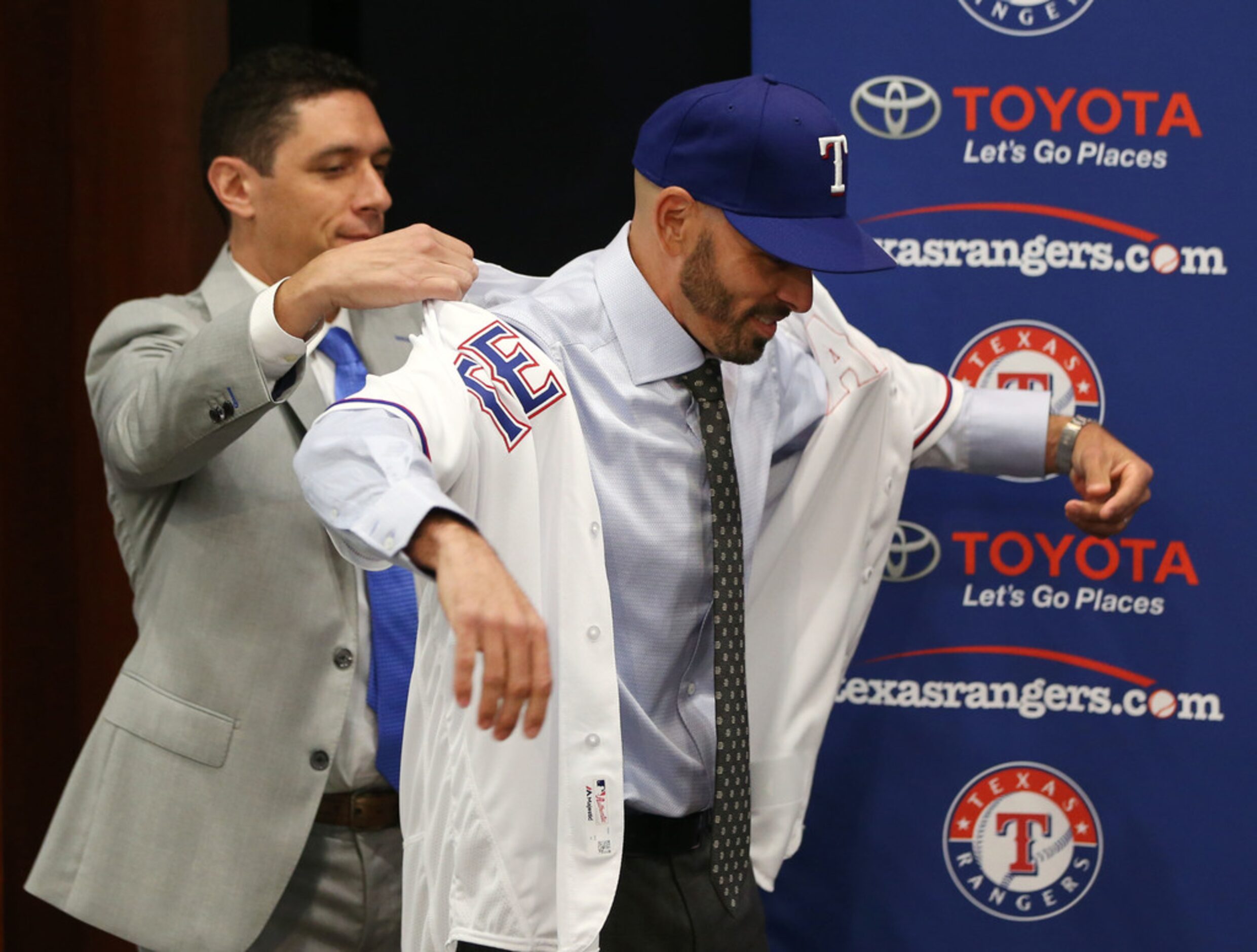 Texas Rangers' new manager Chris Woodward puts on his jersey with help from General Manager...