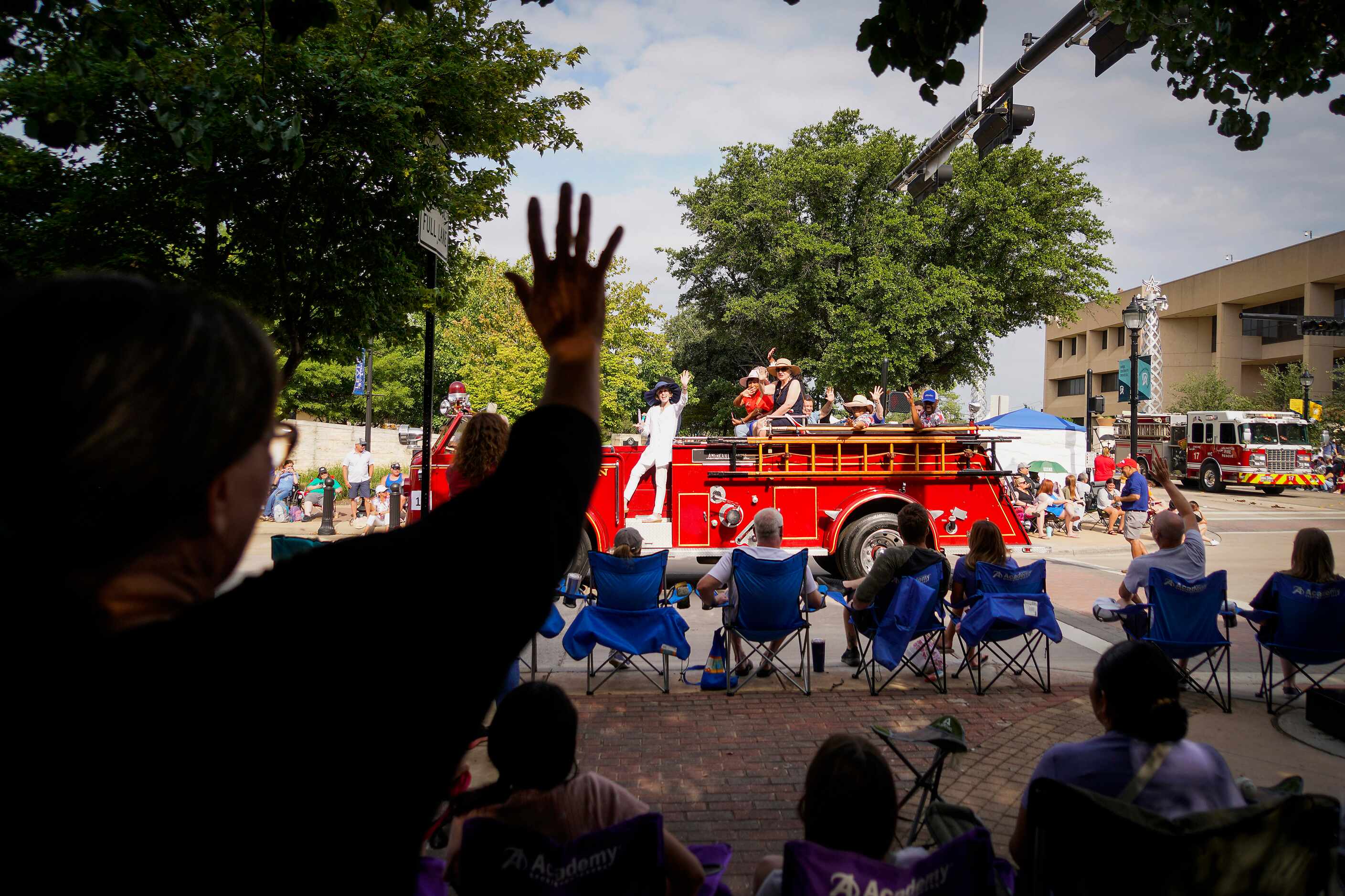 Spectators wave from a shady watching spot during the Arlington Independence Day Parade on...