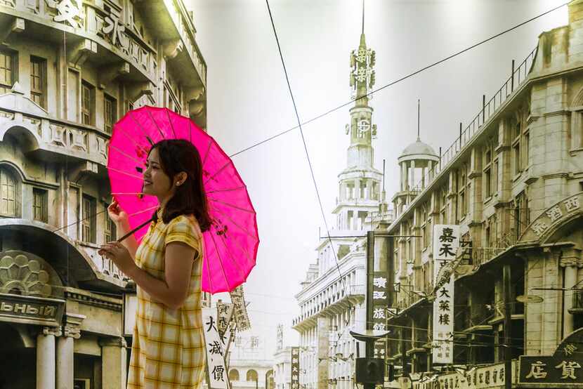 A woman poses in front of a mural made from a historic photo of Shanghai.