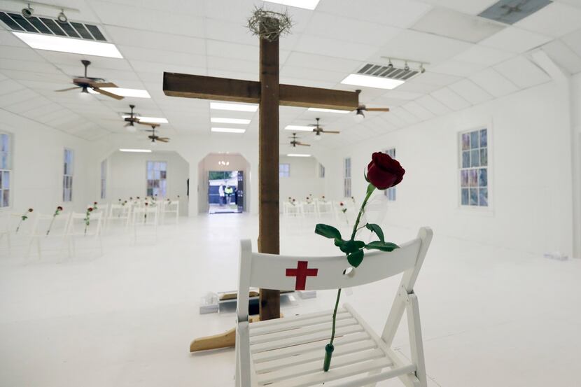 Twenty-six white chairs, each decorated with a rose and a painted cross, sit in the...