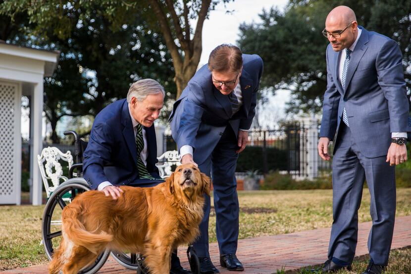 Gov. Greg Abbott (left) and House Speaker Dennis Bonnen pet one of the governor's dogs,...