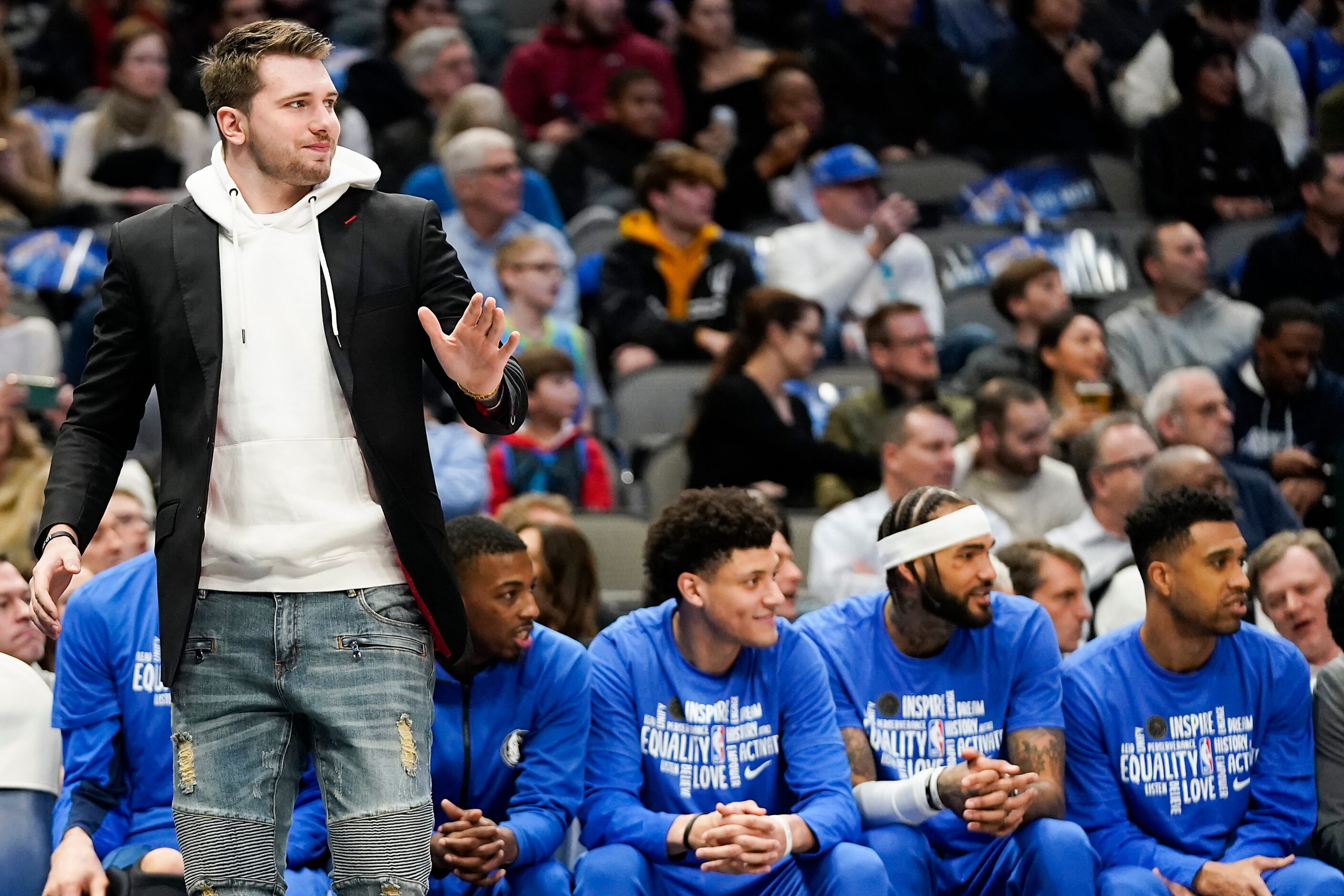 Injured Dallas Mavericks guard Luka Doncic watches from the sidelines in street clothes...