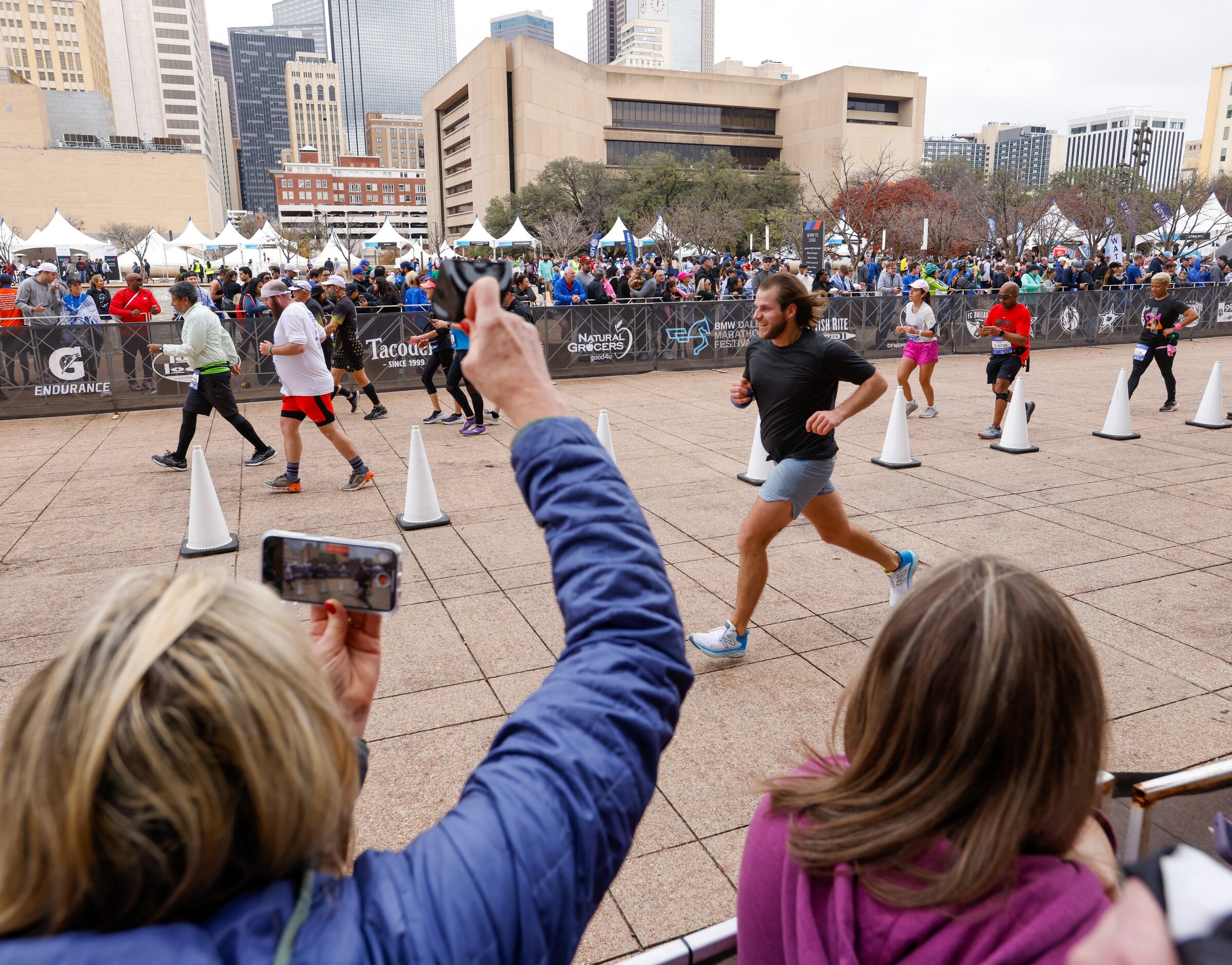 Mary Jacey (left) rings a bell as she cheers for and records her son Ben Jacey (center)...