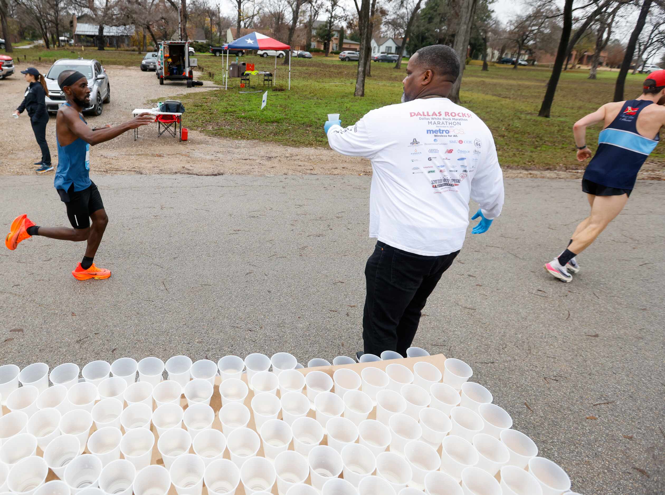 Cliff Piper (center) gives water to runners at the 17-mile mark of the BMW Dallas Marathon...