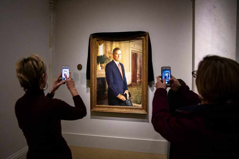 Visitors take photos of the portrait of former President George H.W. Bush, draped in black...
