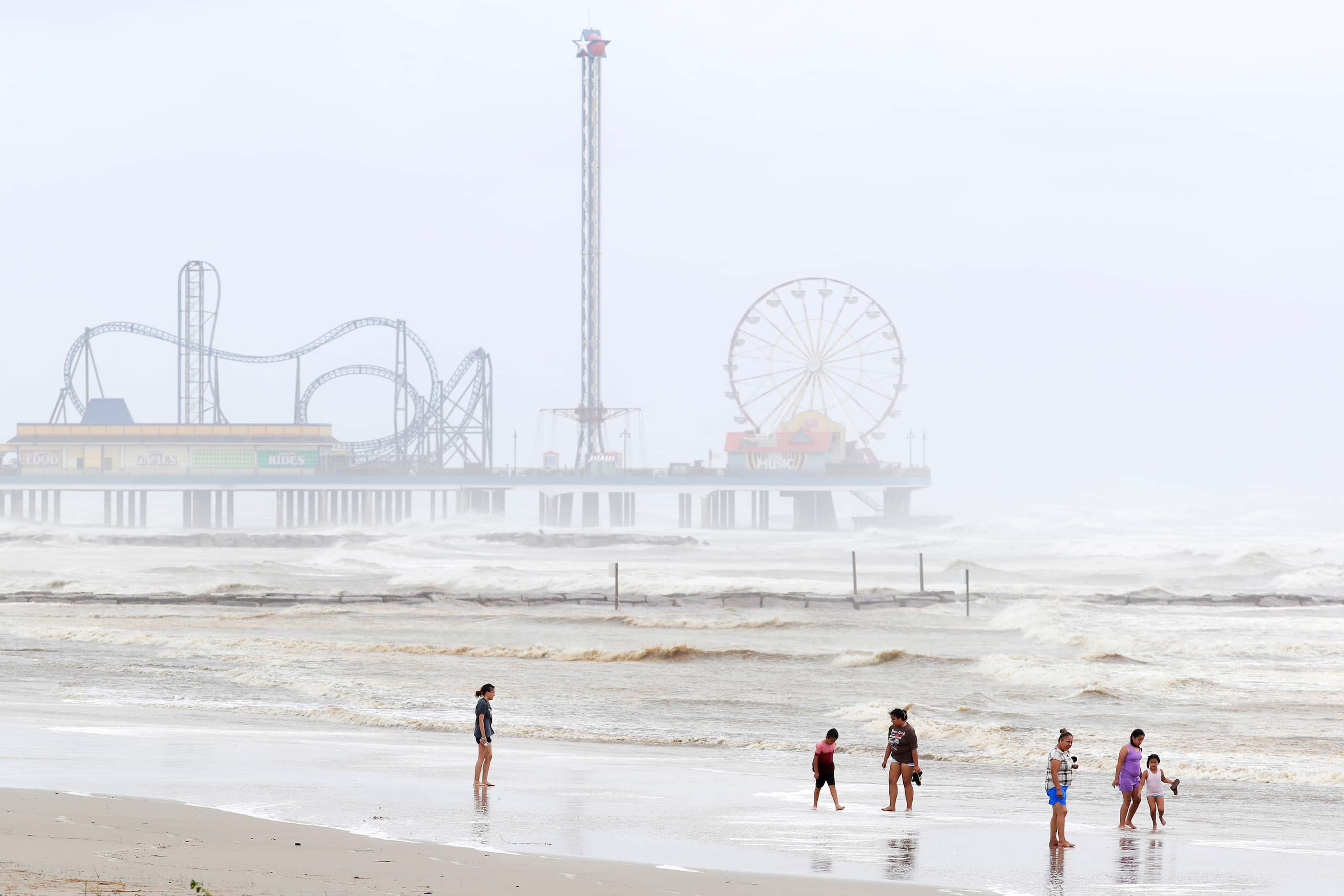 A family walks the beach amid the choppy surf adjacent to Pleasure Pier, in background, as...