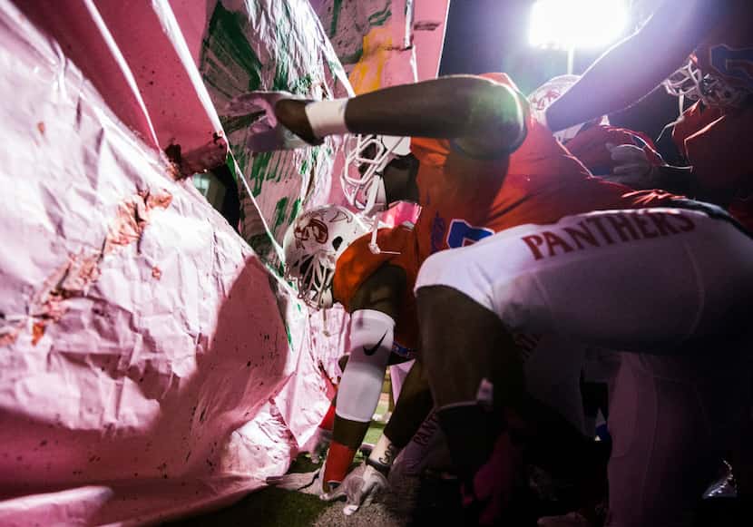 Duncanville football players rip through a paper banner as they enter the field before their...