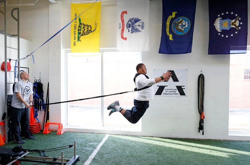 James Castleman leaps  as performance specialist Jonny Wright applies tension during a...