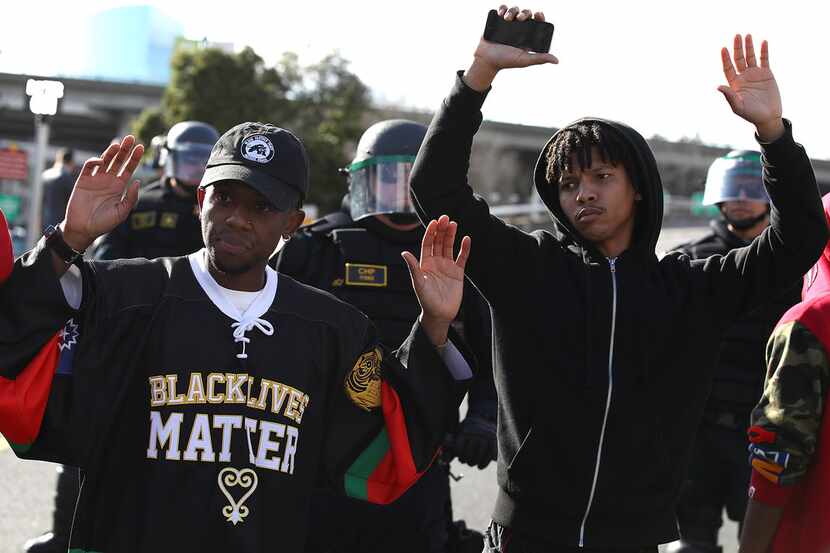 Black Lives Matter protesters stand with their hands up in front of California Highway...