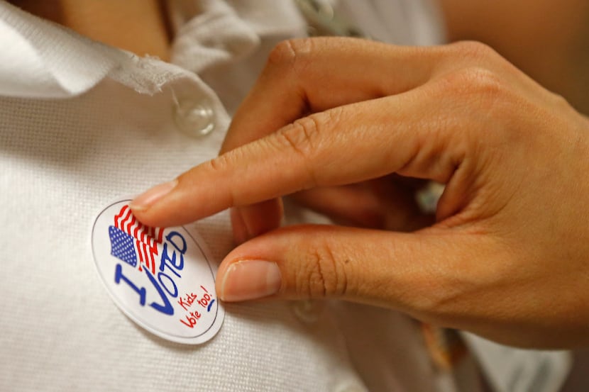 A third-grader receives an "I voted" sticker from a school staff member in a mock election...