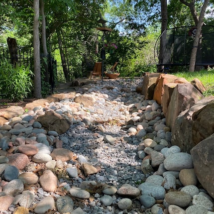 Dry stream bed of rocks in a green backyard with lots of trees