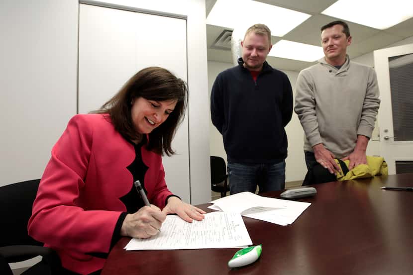Oakland County Clerk Lisa Brown signs a marriage license for Justin Flowers, middle, and...