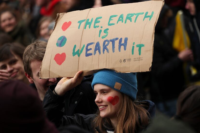 A young woman holds up a board as she marches with others during a climate change protest in...