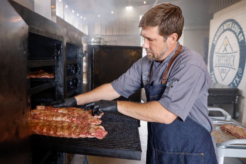 Crossbuck BBQ owner and chef Tim McLaughlin places racks of ribs into a smoker at his...