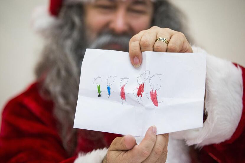Adam Hamner (dressed as Santa)  shows off a drawing included with a letter. Hamner says he’s...