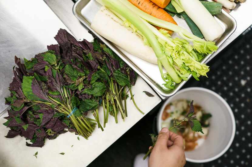 Khao Noodle Shop employee preps vegetables, dropping unusable scraps into a bucket provided...