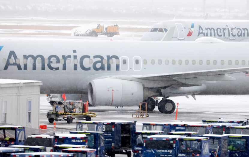 Ground crews plow sleet and snow from the runway so American Airlines jets parked at...