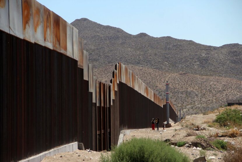 A Mexican family stands next to the border wall between Mexico and the United States, in...