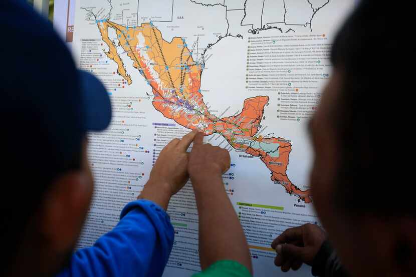 Migrants discuss their journey using a map posted inside the sports complex where thousands...