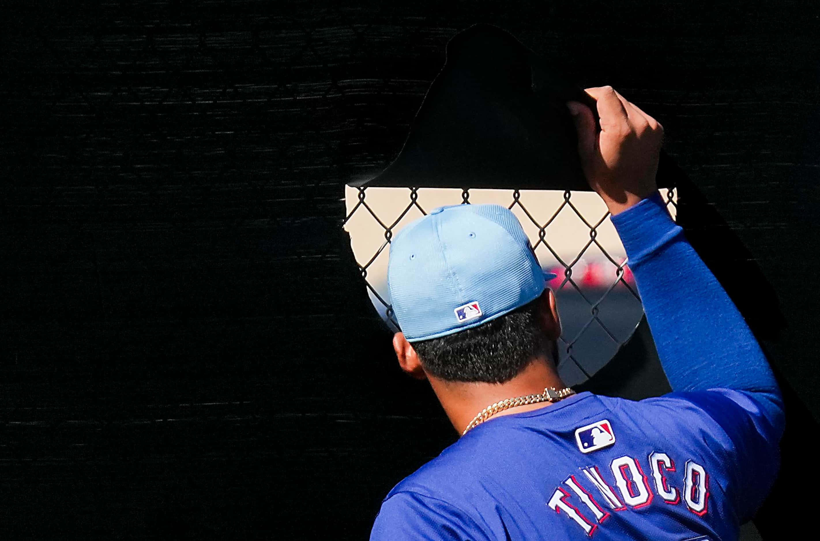 Texas Rangers pitcher Jesús Tinoco peeks through a practice field fence during a spring...