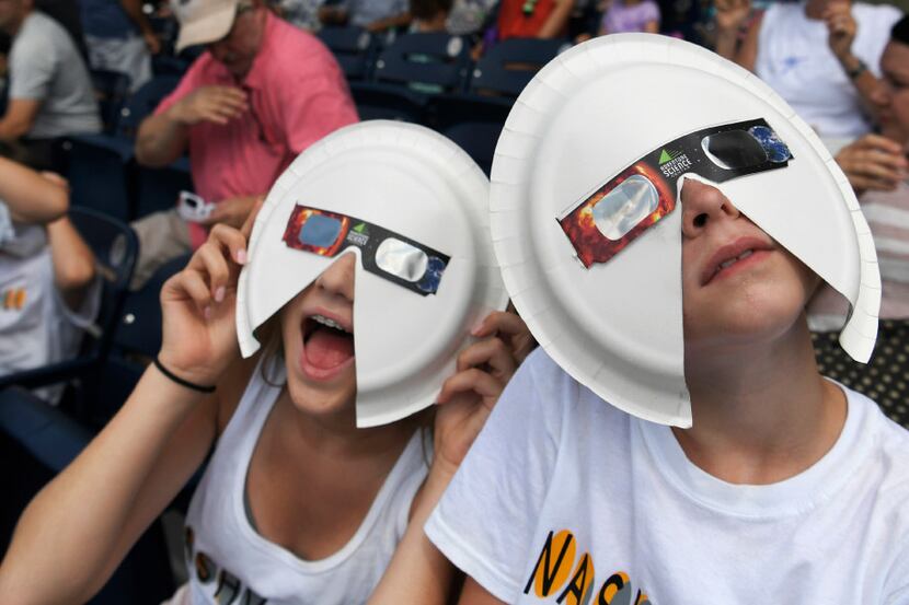 Annie Gray Penuel and Lauren Peck, both of Dallas, wear their makeshift eclipse glasses at...
