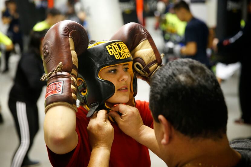 Garland High School student Annalicia Sustaita has her helmet tightened by her father Ray...