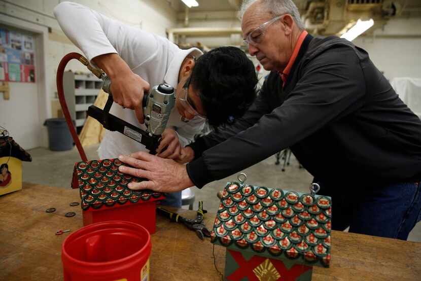 Sophomore Servando Badillo works with shop teacher Doug Palmer to affix bottle caps for the...