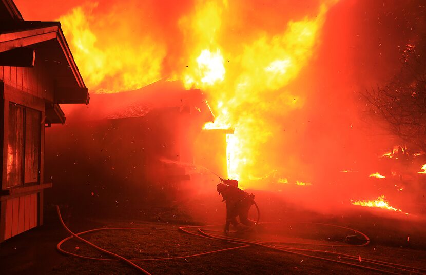 A Cazadero firefighter struggles to protect a home from catching fire in Coffey Park, Monday...