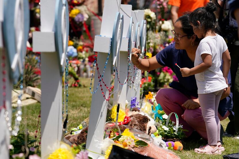 A woman signs a cross as a child looks on at a makeshift memorial by the mall where several...