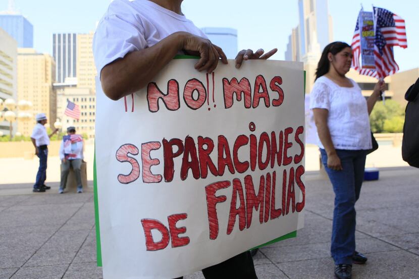 A woman holds a sign that reads "Stop separating families" while listening to activists...