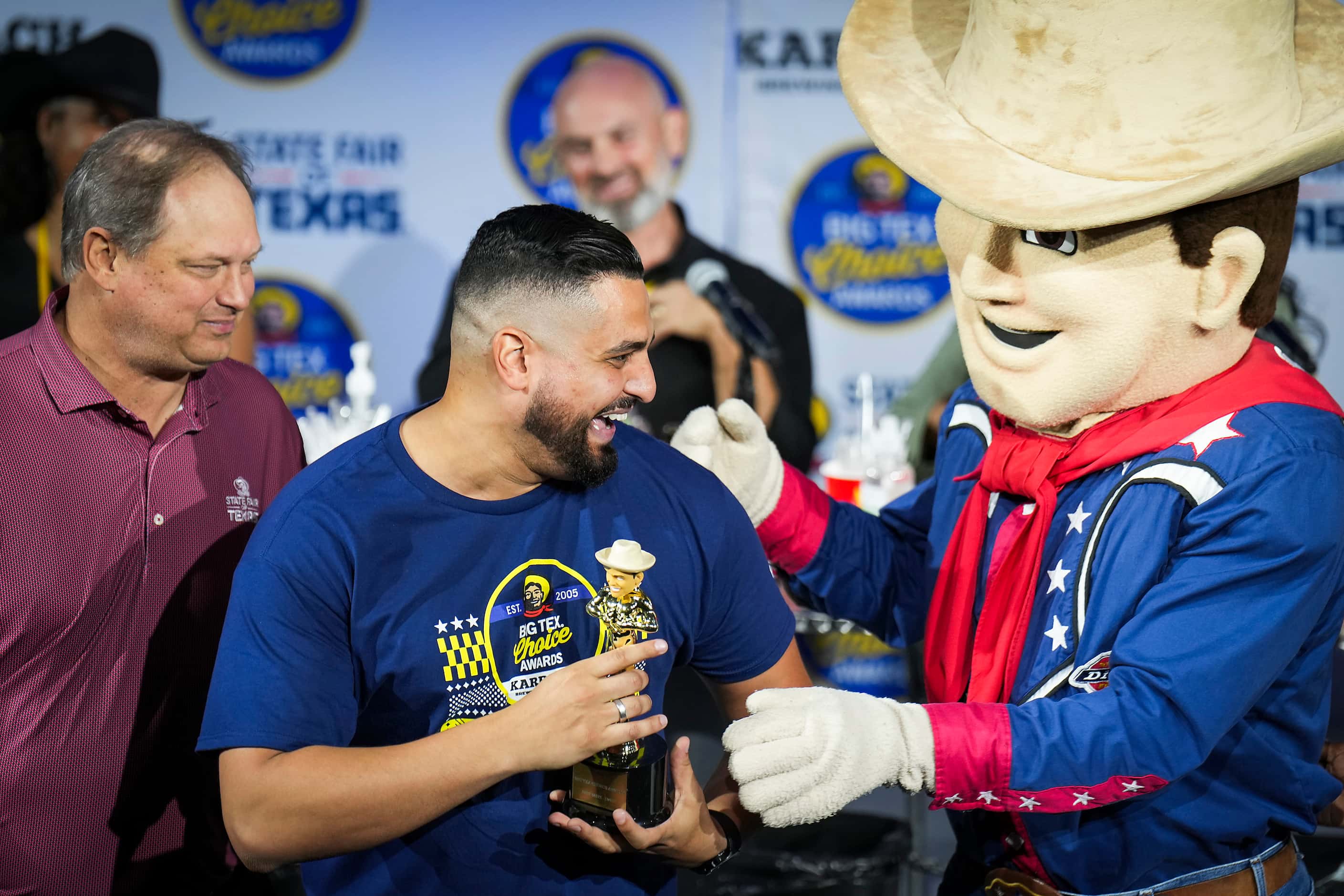 Stephen El Gidi is presented a trophy by mascot Little Big Tex after he won ‘best taste -...