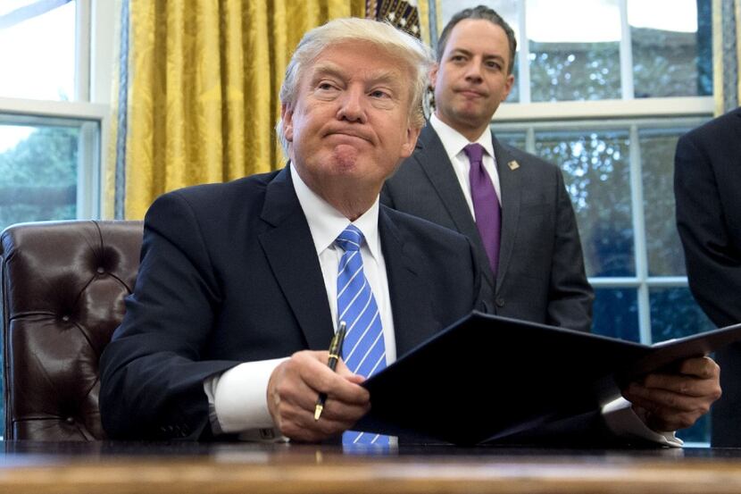 US President Donald Trump signs an executive order as Chief of Staff Reince Priebus looks on...