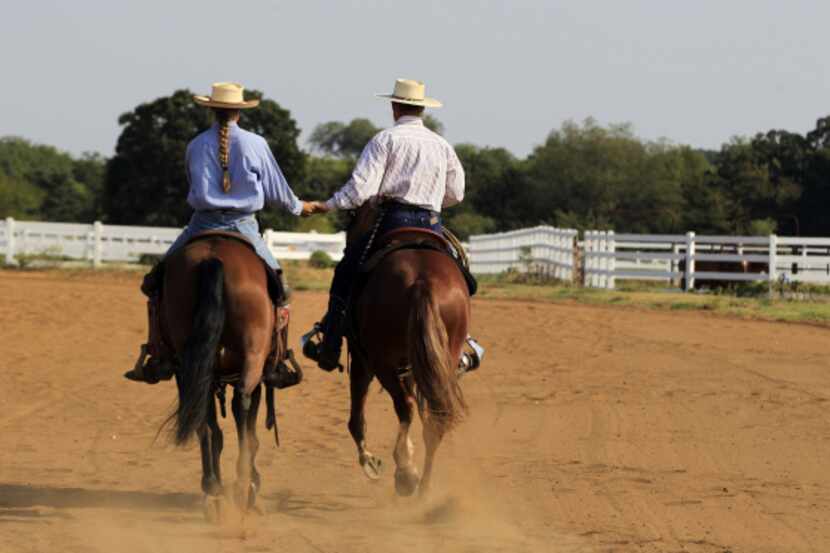 Miranda and Mark Lyon hold hands as they ride their mustangs, Atlas and Huckleberry, at Kyle...