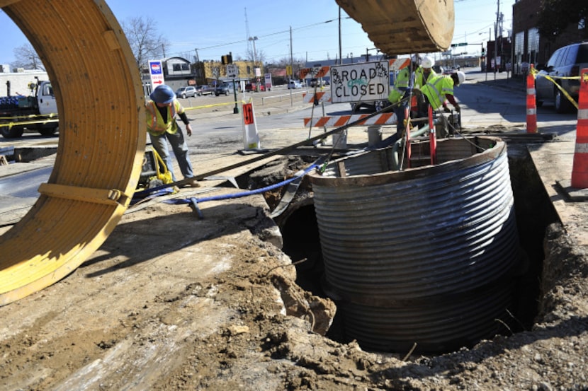 Construction workers work to install a manhole at the intersection of Malcolm X Boulevard...