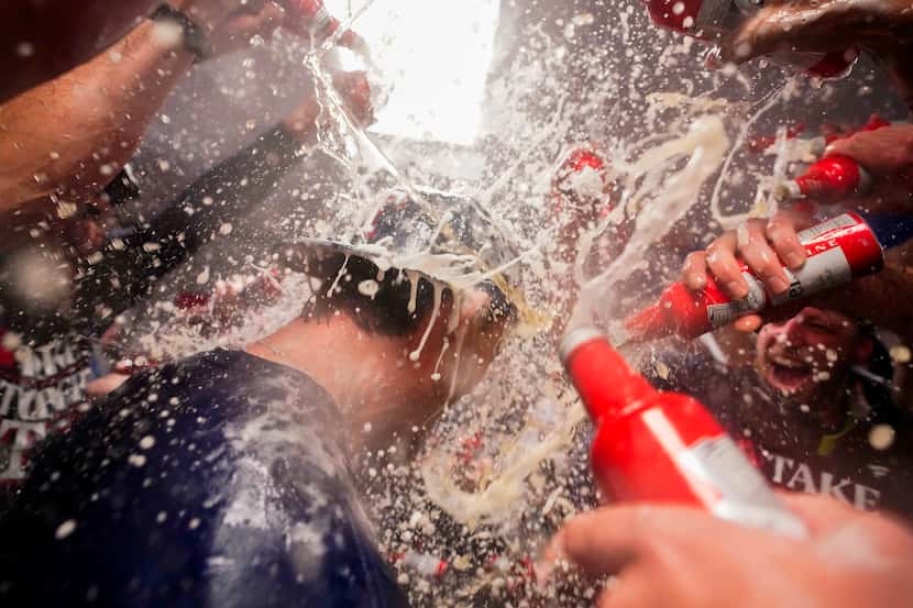 Texas Rangers left fielder Evan Carter is doused with beer and champagne by teammates in the...