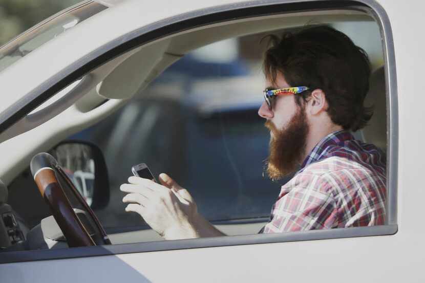 A man works his phone as he drives through traffic in Dallas on Feb. 26, 2013.