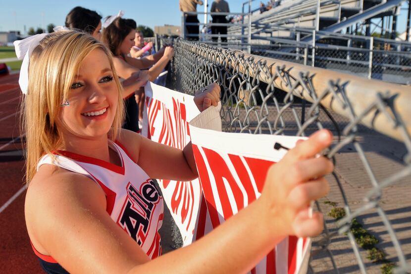 Allen junior cheerleader Ashley Mehmken hangs spirit signs before a high school football...