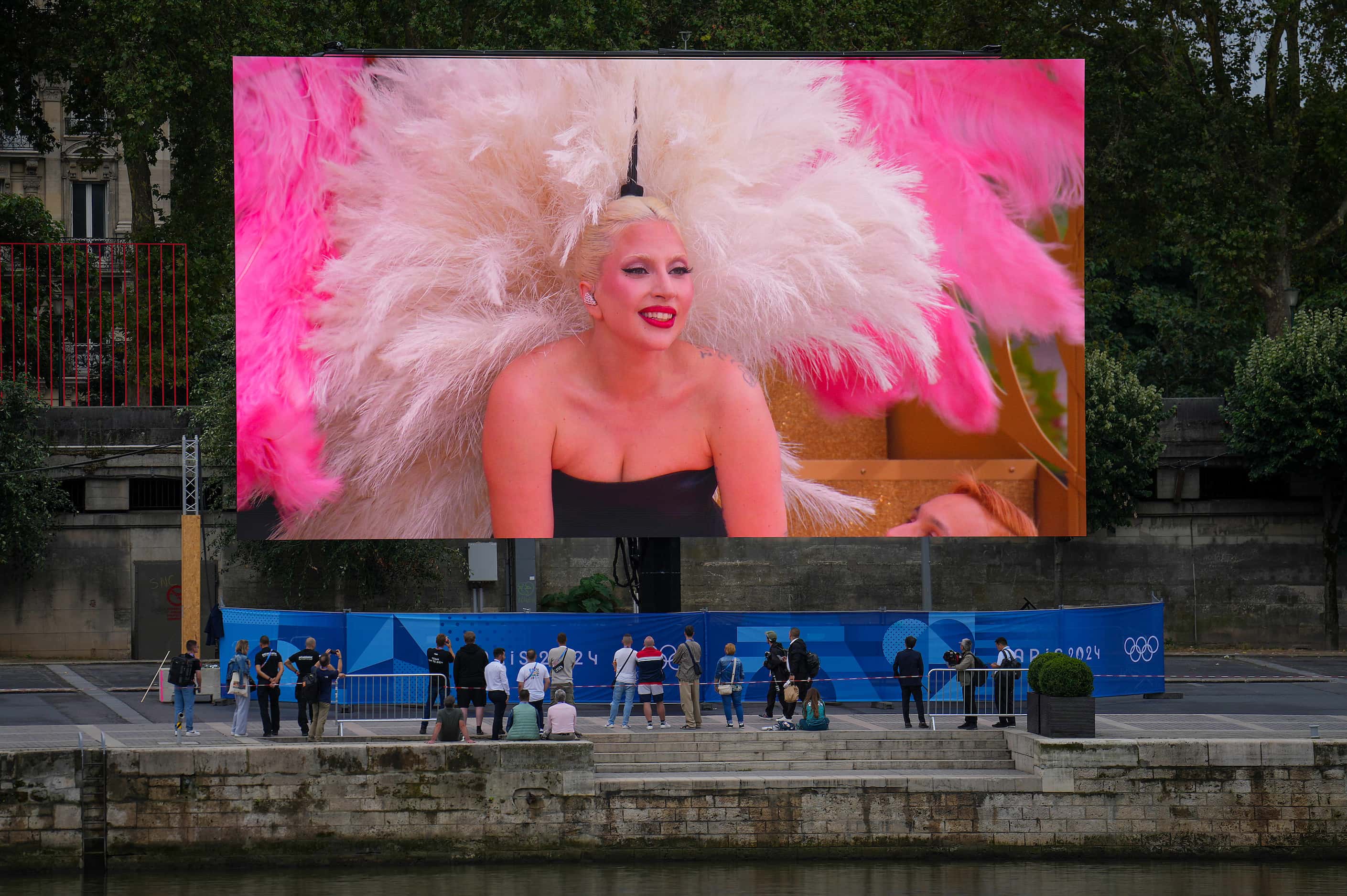 People watch a large screen along the Seine as Lady Gaga performs performs during opening...